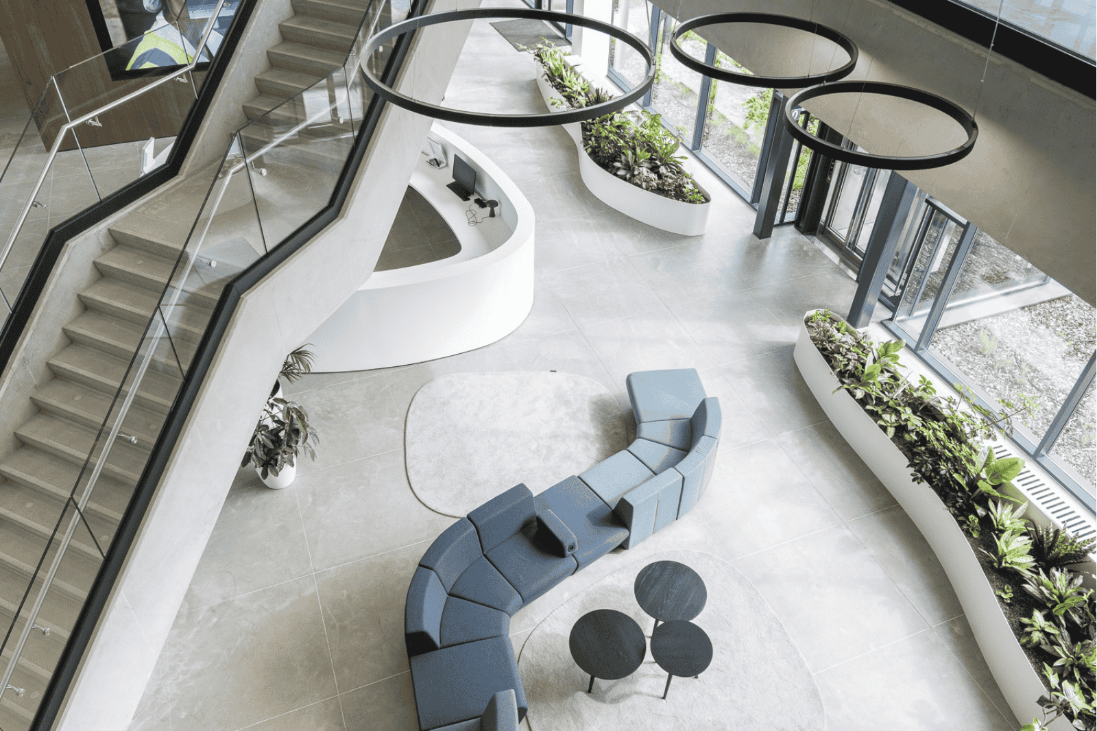 Office design by Buro Project featuring a bright reception area with stairs, large windows, greenery, and a lounge setup.